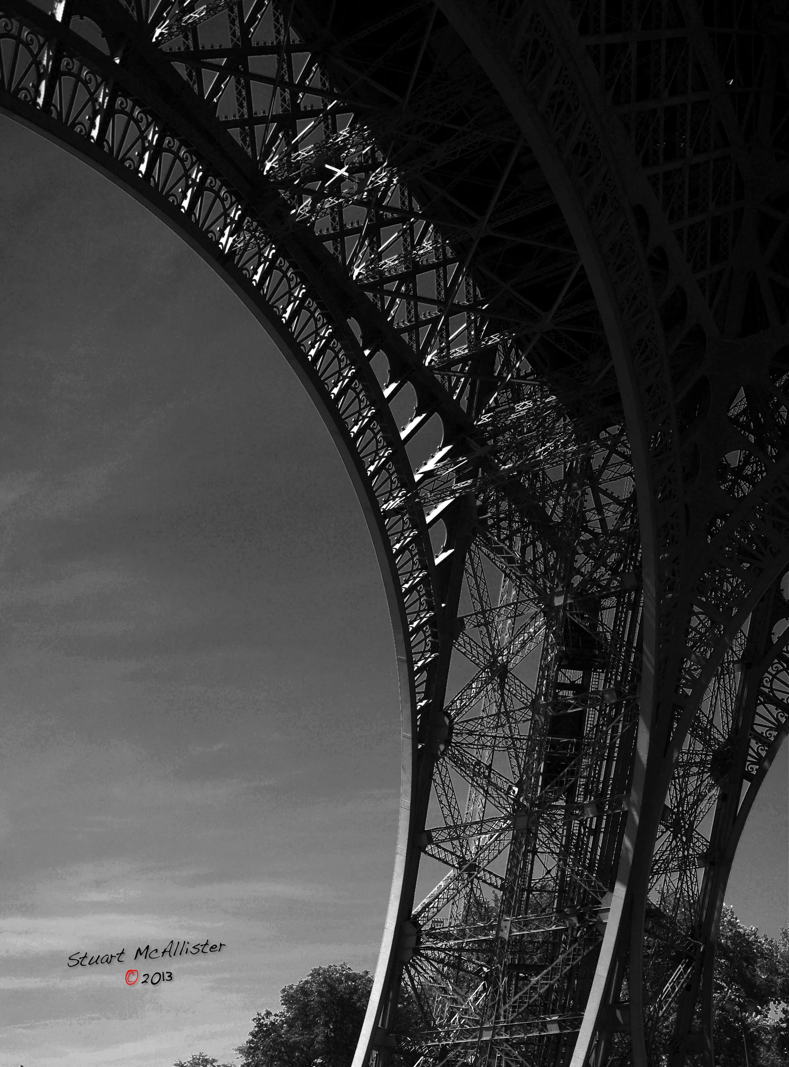 The underside of a large steel bridge curves across a cloudy sky.