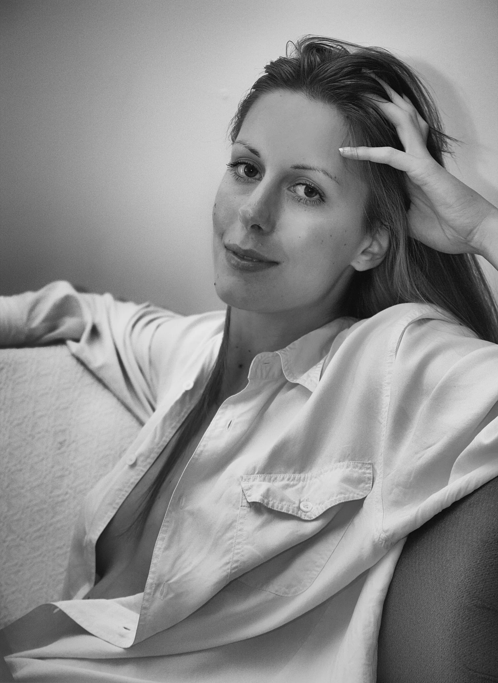 A relaxed monochrome seated portrait with one hand raised to the forehead.