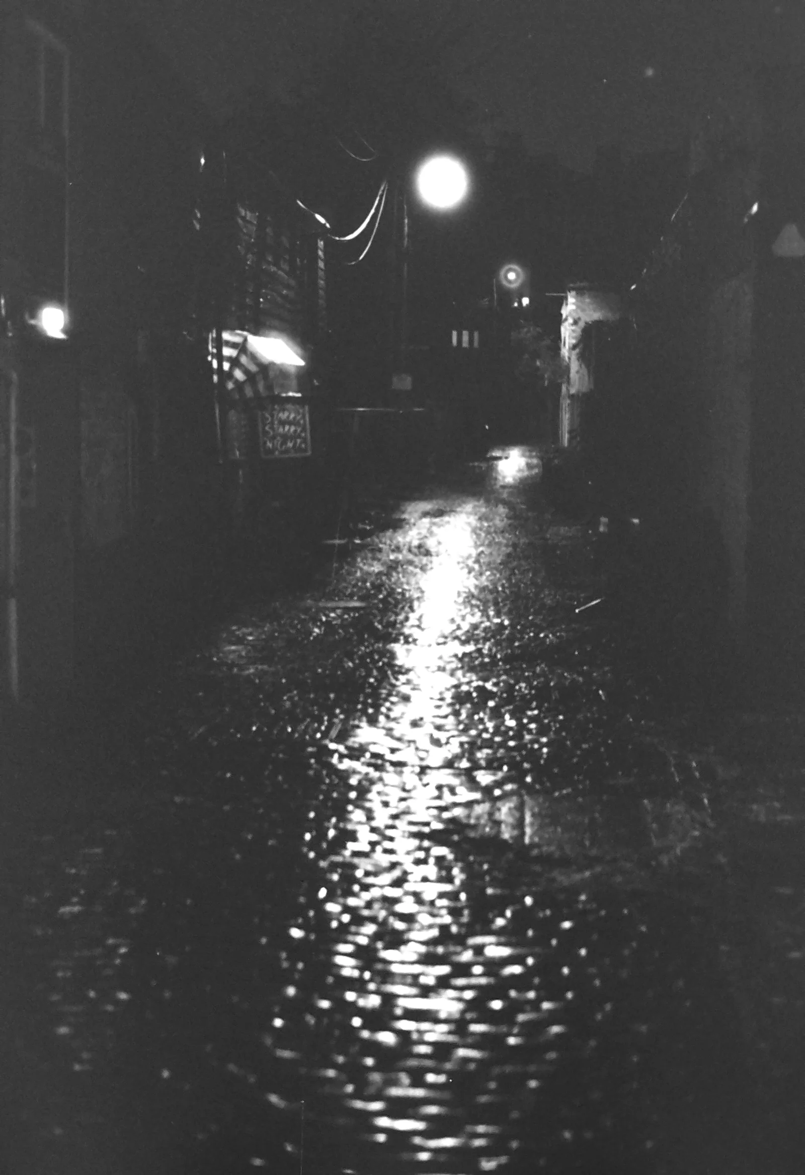 Streetlight reflects across an empty wet road at night.