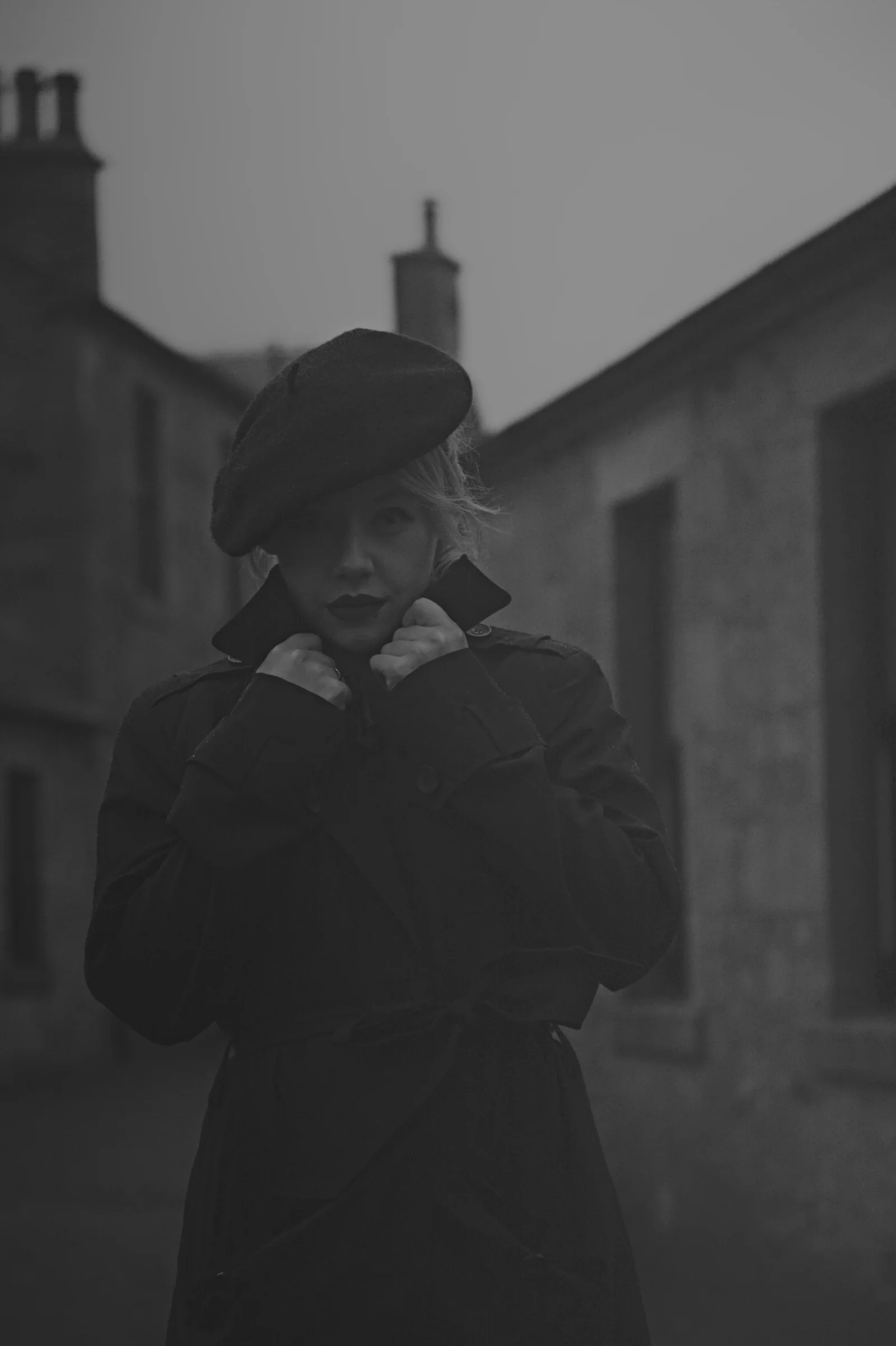 A solitary figure in a coat and hat stands in a misty street.