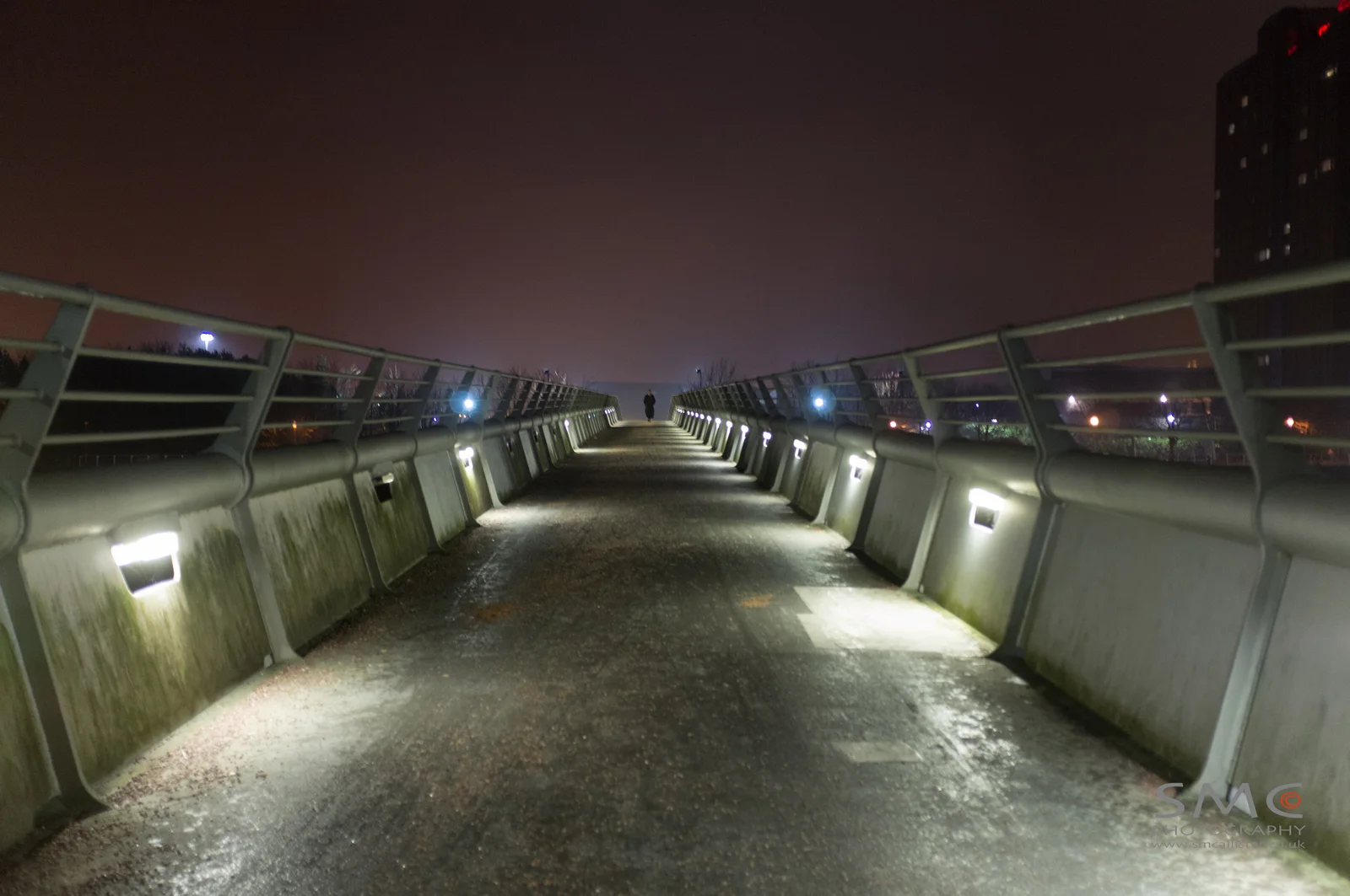 An empty illuminated bridge extends into the night.