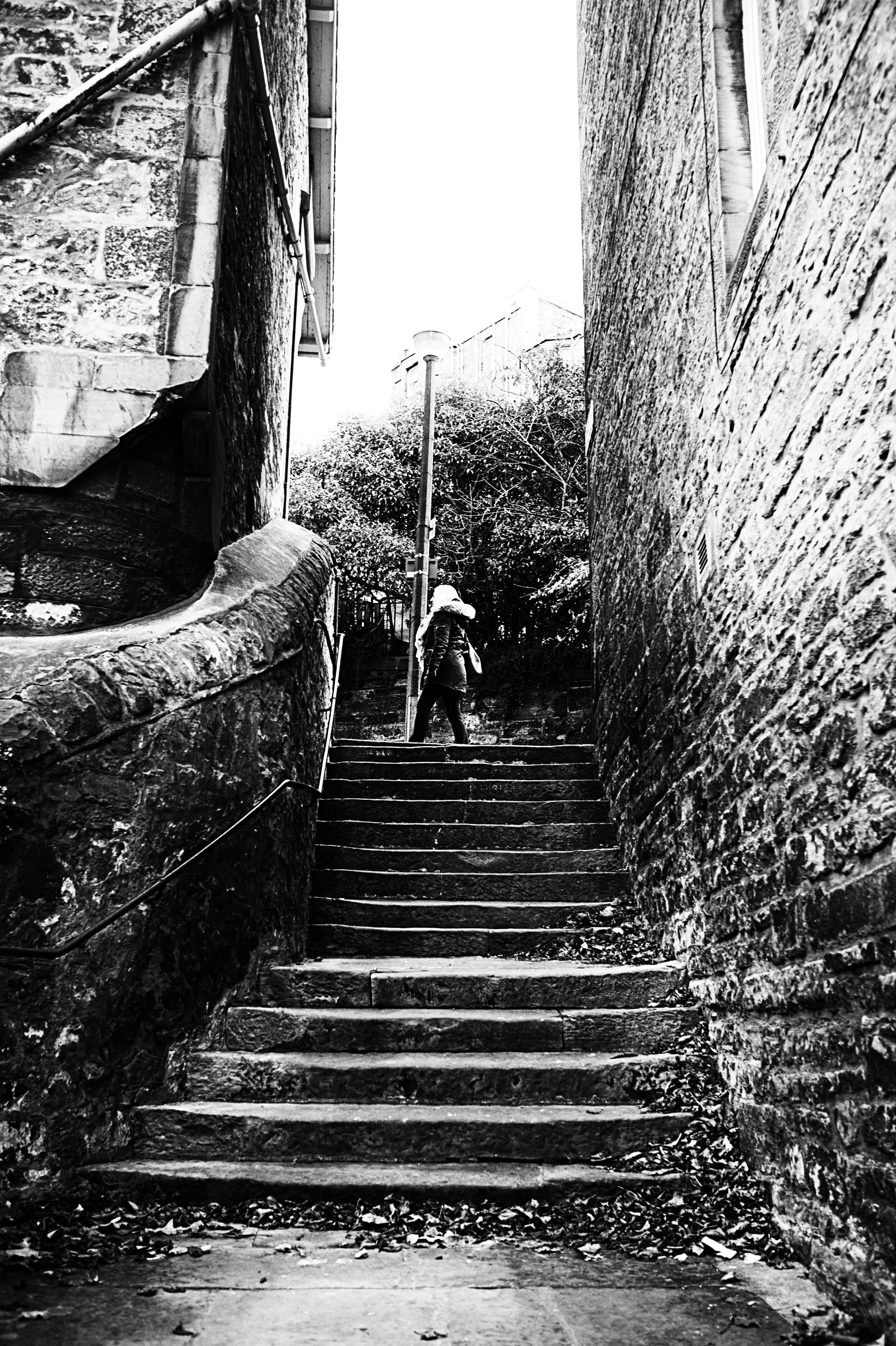 A distant person climbs old stone steps between tall walls.