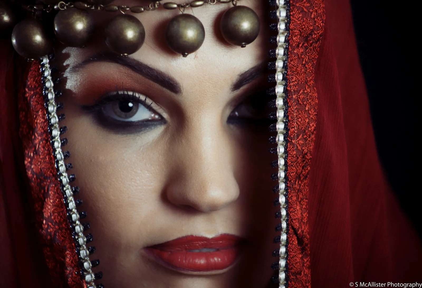 A close portrait framed by red fabric and metallic ornament.
