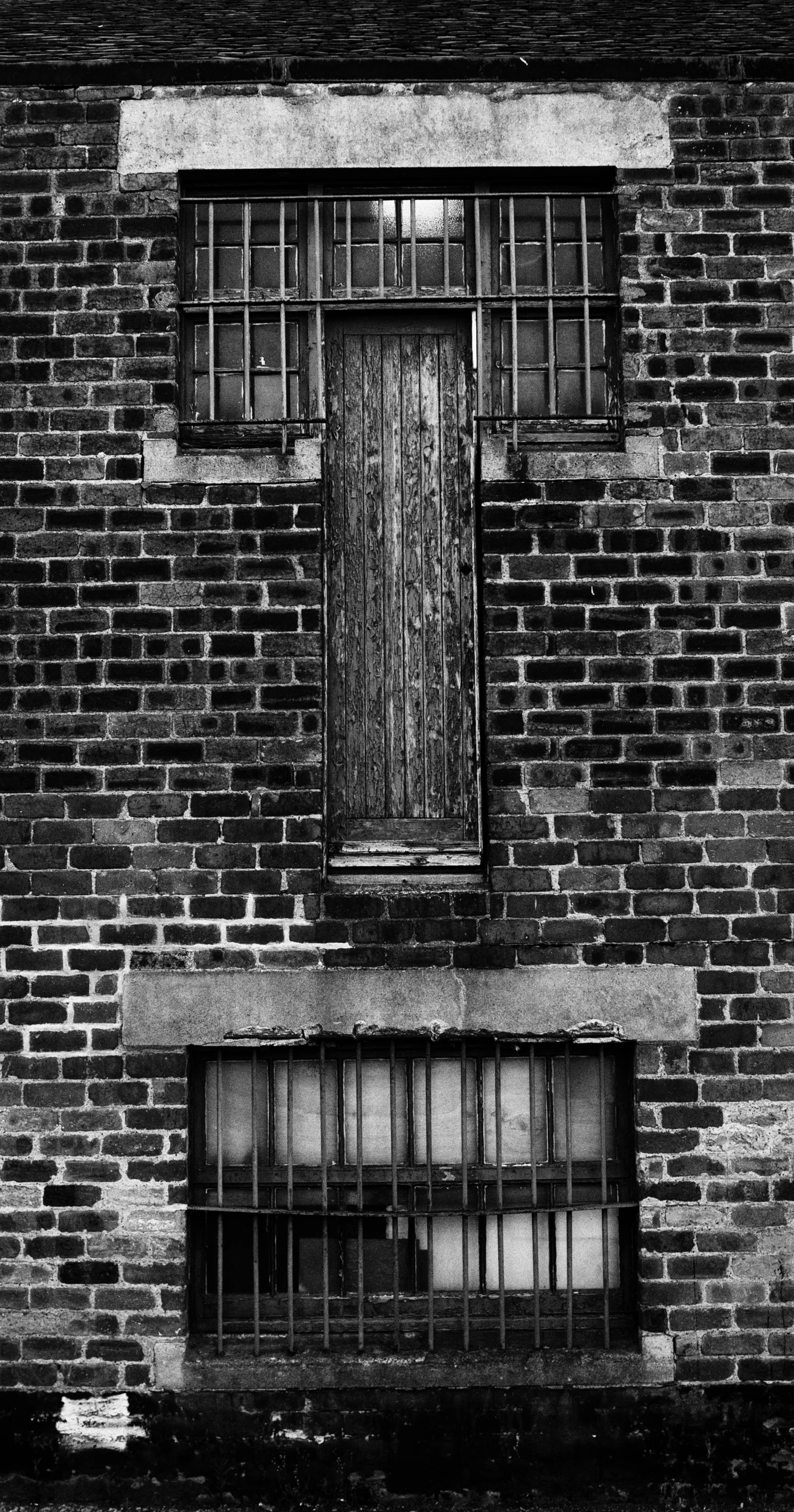 A sealed door and windows remain in a weathered brick wall.