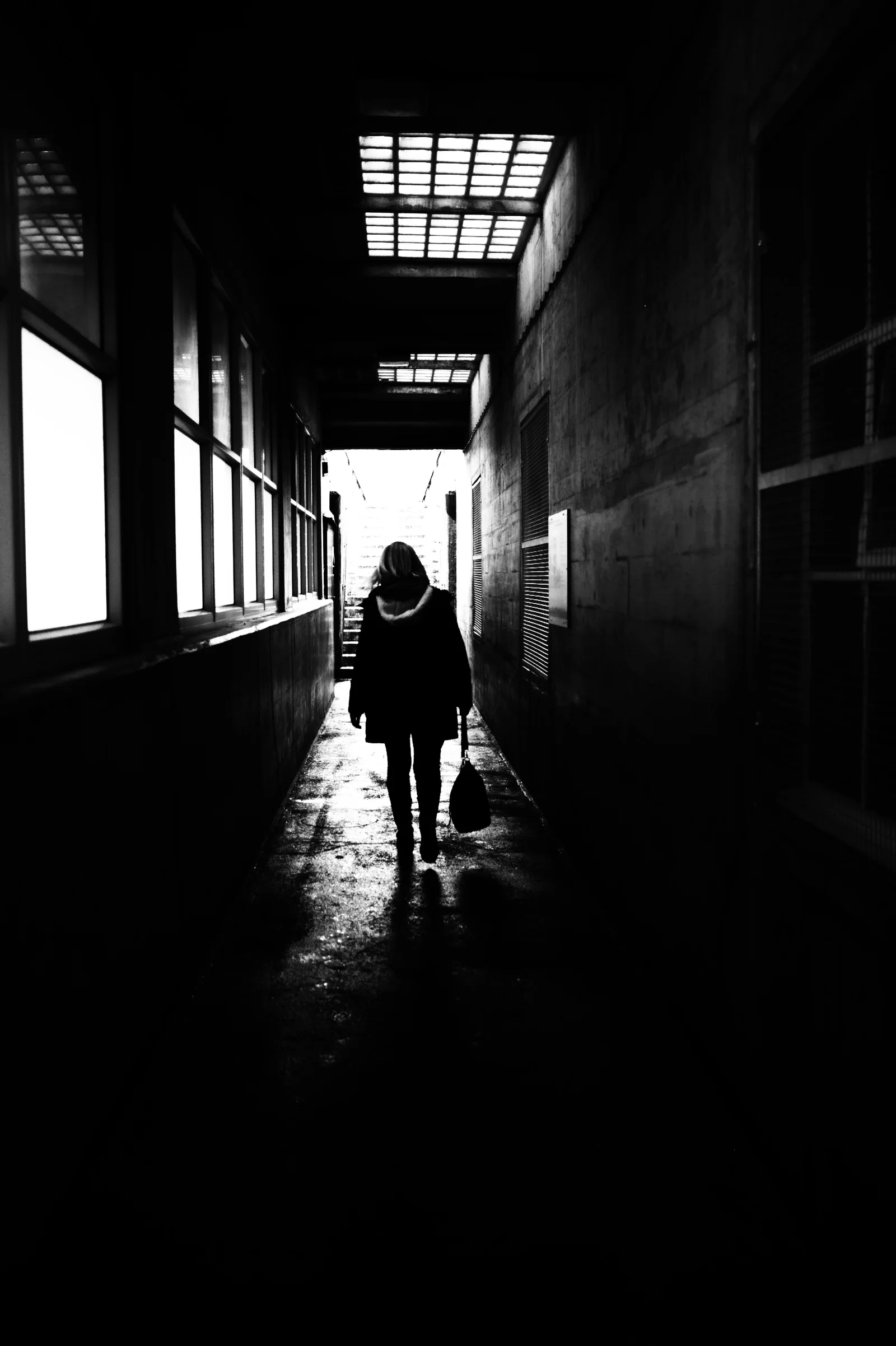 A distant figure leaves through a high-contrast corridor.