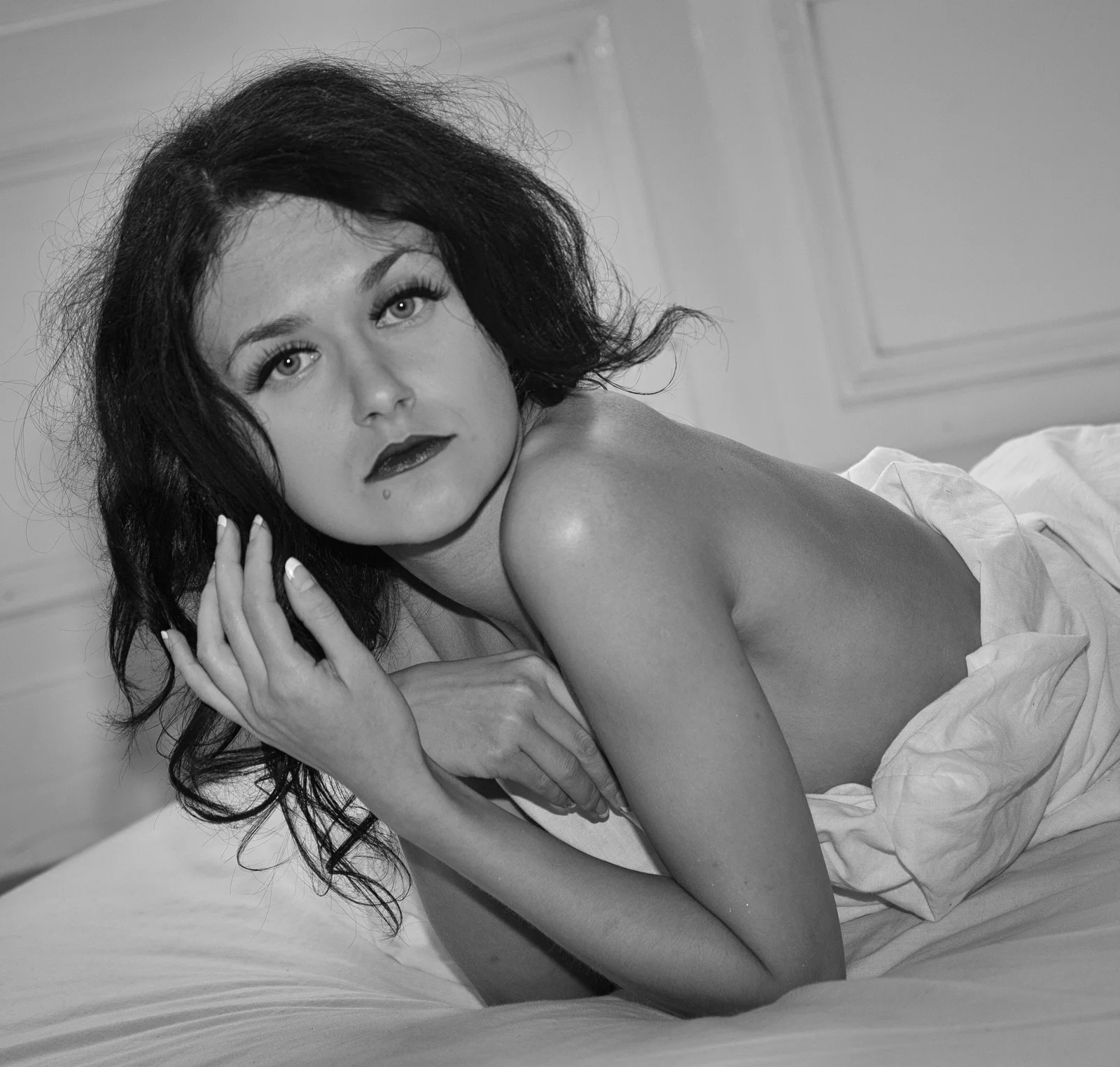 A reclining woman looks toward the camera from a bed.